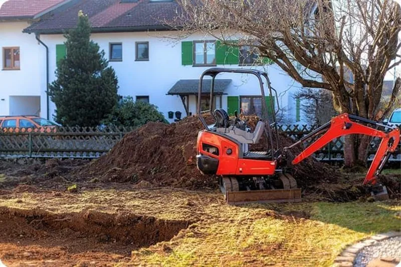 An excavator standing in a garden being used to dig a hole